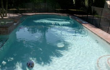 fenced backyard swimming pool with brick paver patio