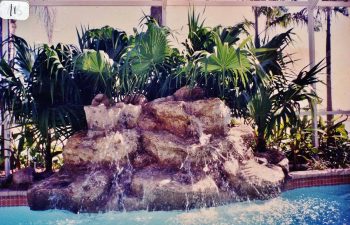 glass enclosed swimming pool with a hardscape waterfall