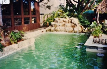 backyard swimming pool with green water color and a hardscape waterfall