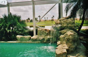 glass enclosed swimming pool with a hardscape waterfall