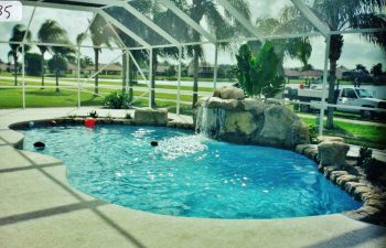 glass enclosed swimming pool with a hardscape waterfall