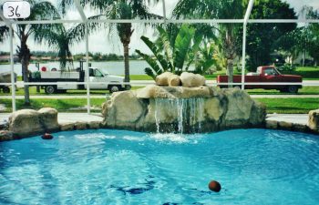 glass enclosed swimming pool with a hardscape waterfall