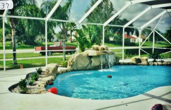 glass enclosed swimming pool with a hardscape waterfall