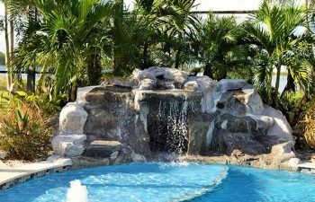 garden indoor swimming pool with a hardscape waterfall and palms by the pool edge