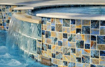 backyard swimming pool with waterfalls coming down walls with decorative tiles