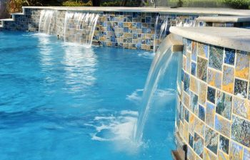 backyard swimming pool with waterfalls coming down walls with decorative tiles
