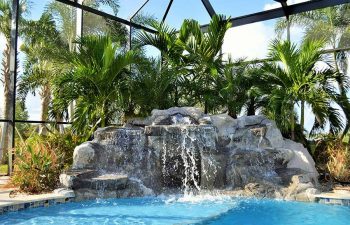 garden indoor swimming pool with a hardscape waterfall and palms by the pool edge