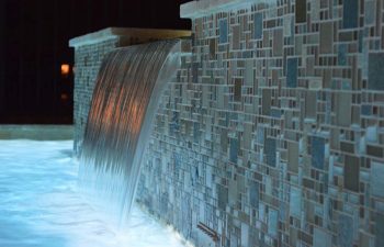 ackyard spa pool with a waterfall and decorative tiles