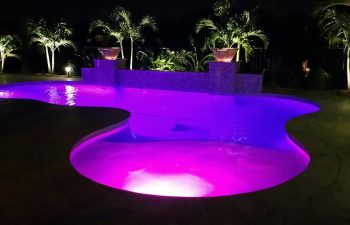 night view of a backyard swimming pool with a purple lighting