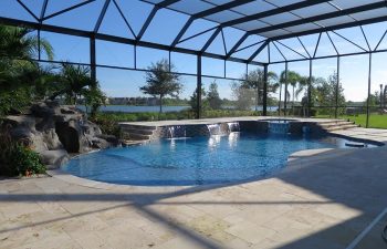 glass enclosed swimming pool with waterfall and hardscapes