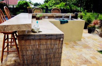 outdoor kitchen with a bar and stools on a backyard swimming pool patio