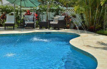 outdoor furniture by a backyard swimming pool with fountains