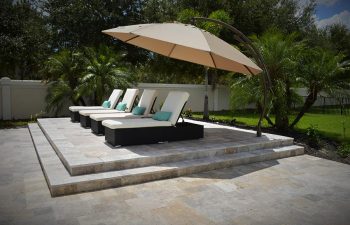 four sunbeds and umbrell on a backyard paver patio