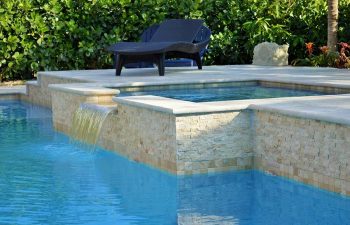 sunbed by a backyard swimming pool with water features and waterfall