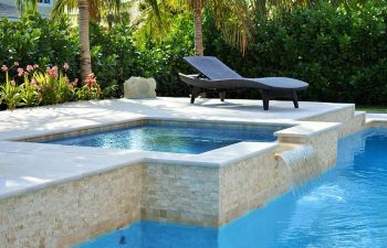 sunbed by a backyard swimming pool with water features and waterfall