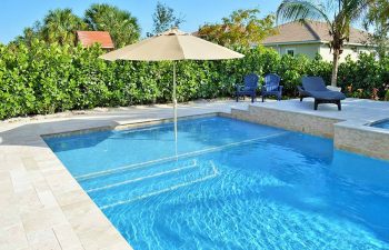 backyard swimming pool with sun umbrella and sunbeds on a deck