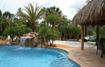 outdoor spa zone with tiki house and a hardscape waterfall on the edge of the swimming pool