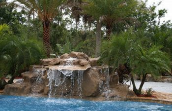 a backyard swimming pool with waterfall and hardscapes