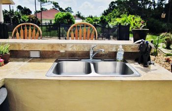 outdoor kitchen with a bar and stools on a backyard swimming pool patio