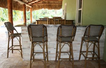 an oudoor bar with stools on a paver patio shaded by a tiki roof