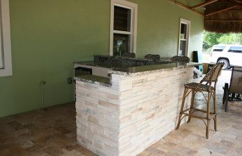 outdoor kitchen with bar and stools under tiki roof