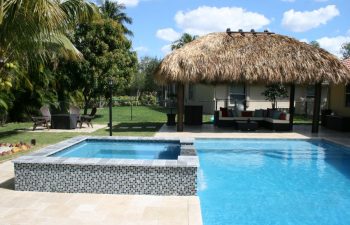 outdoor furniture in a tiki hut by a backyard swimming pool