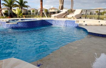 sunbeds on a patio by a backyard swimming pool with jacuzzi and waterfall