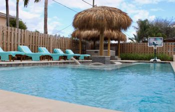 Tiki hut and sunbeds by a backyard swimming pool