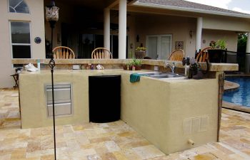 outdoor kitchen with a bar and stools on a backyard swimming pool patio