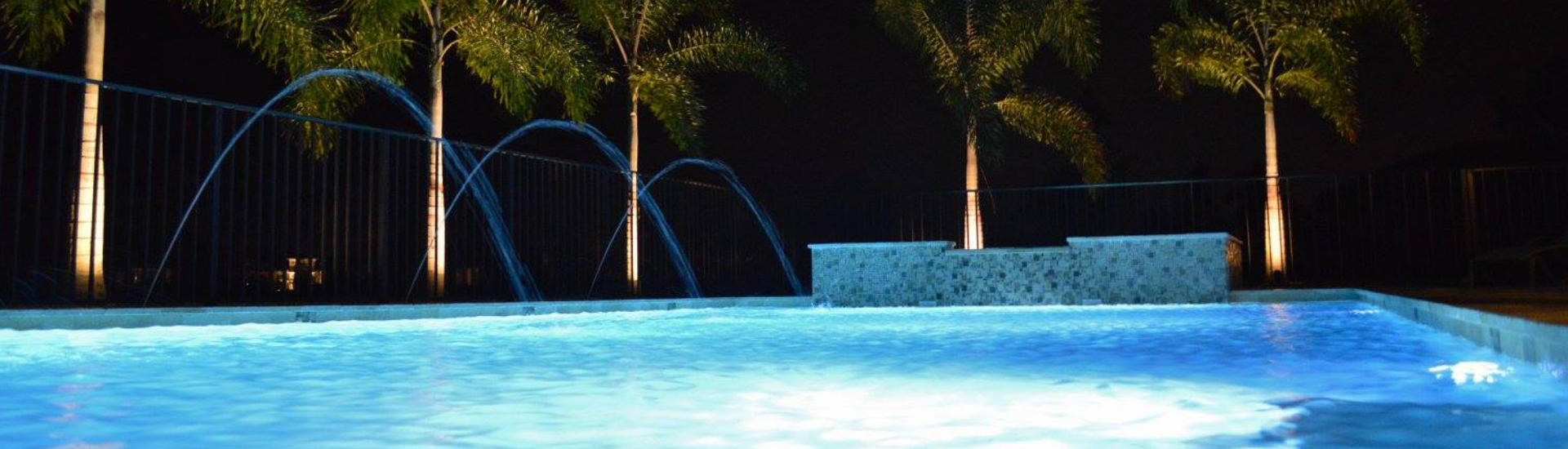 night view of a lit backyard swimming pool with fountains